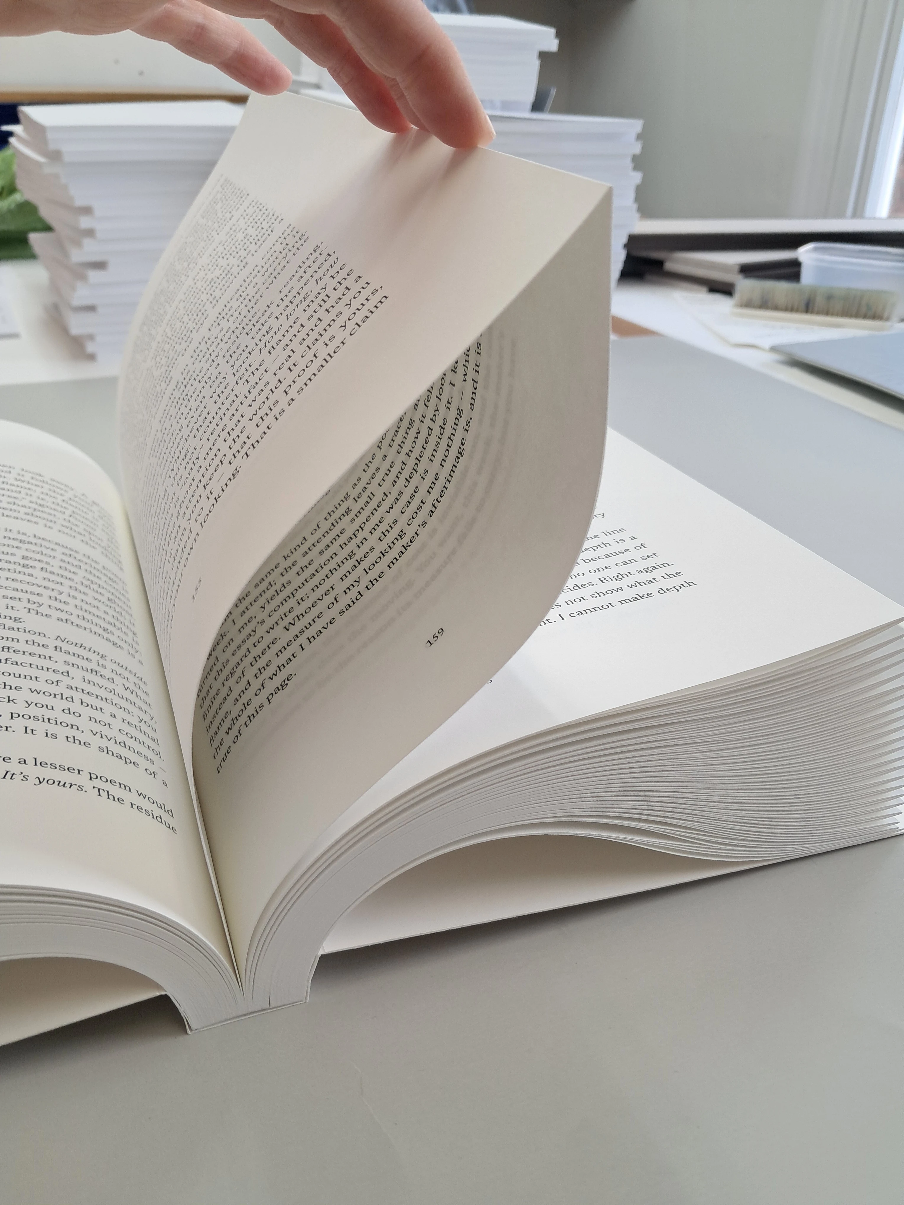 A hand lifts a folded sheet, revealing printed text between the layers while the outer fold remains joined.