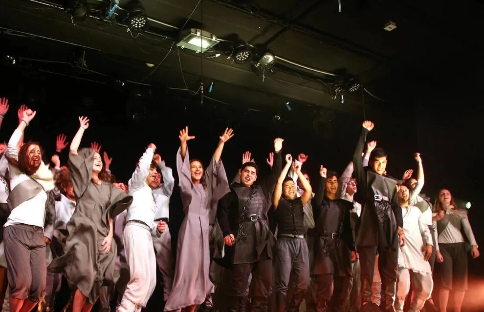 The Hoch Hinaus company mid-jump in the finale — grey robes and armor under stage light.