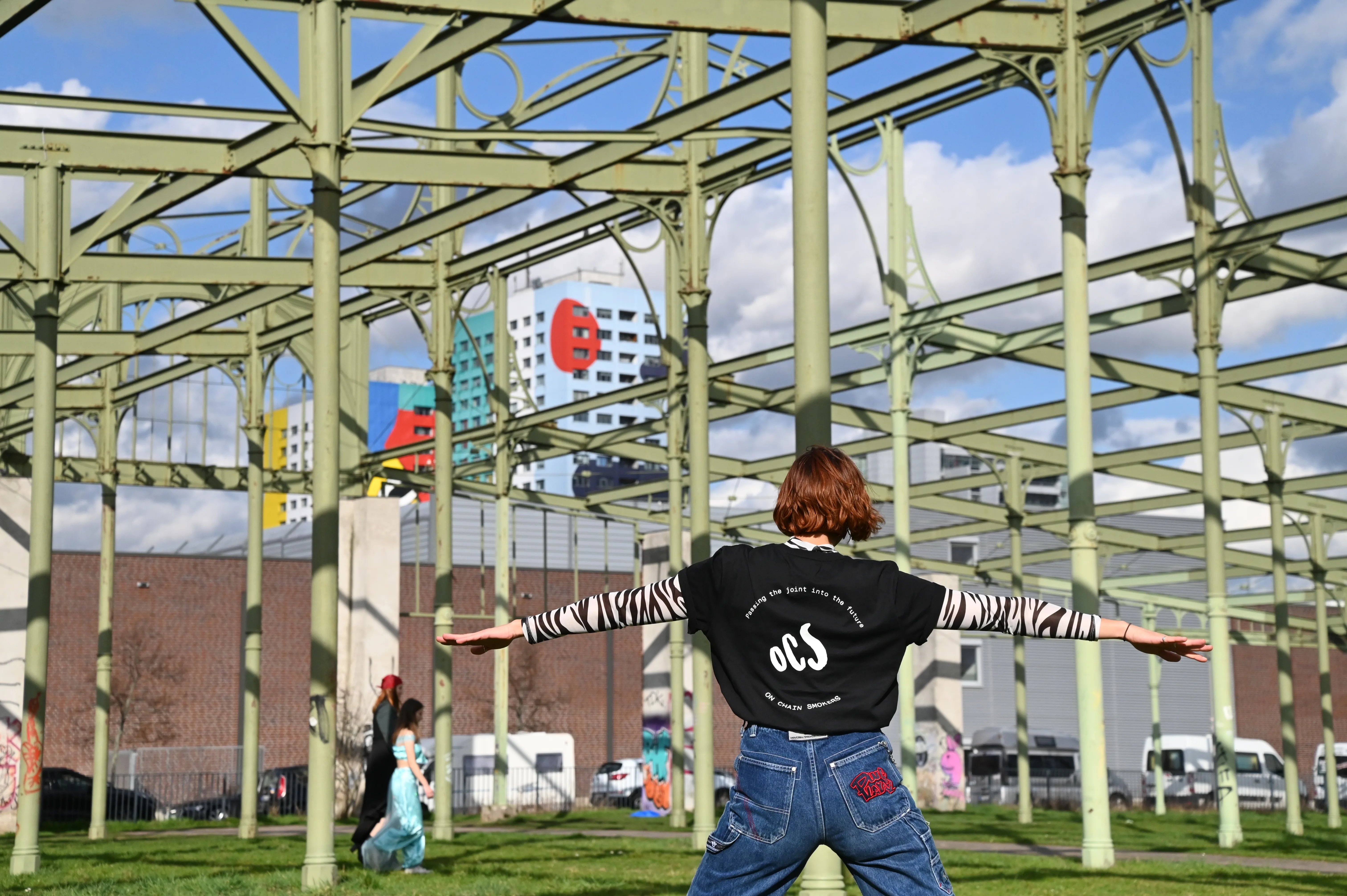 OCS merch worn — the wordmark across the back, arms open in an urban park.